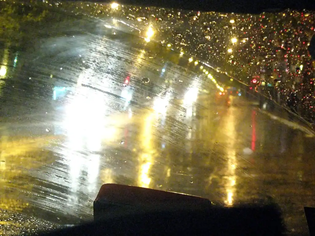 Blurred view of a rainy night through a car windshield with water droplets on the glass.