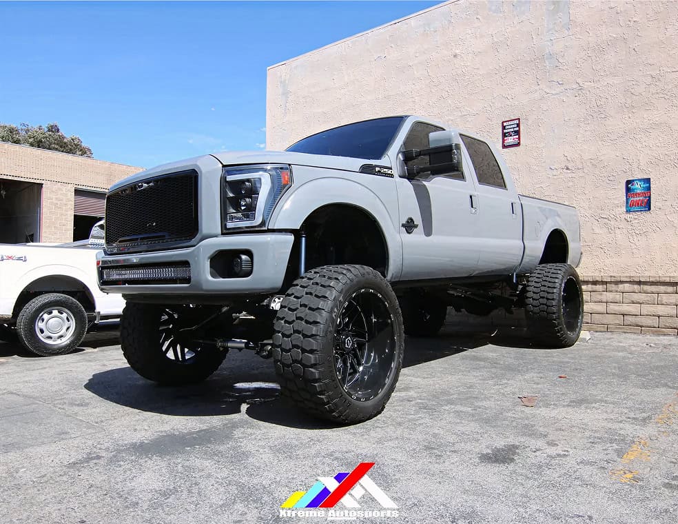 Lifted gray pickup truck with large off-road tires in parking lot.