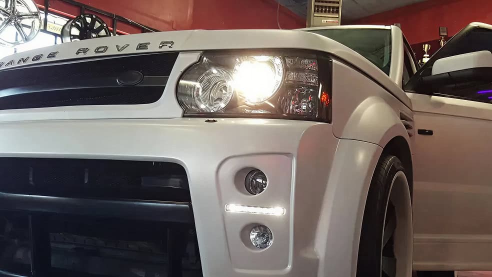 Range Rover SUV front close-up at car dealership showroom glowing headlights and sleek white exterior.