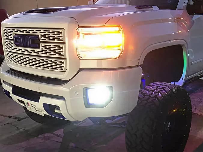 Off-road truck with custom large tires and bright LED lights in a nighttime setting.
