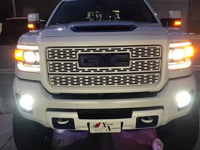 GMC truck front view with illuminated headlights and custom license plate in dark setting.