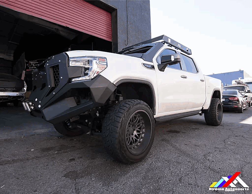 Off-road lifted white truck with aftermarket black front bumper and large tires.