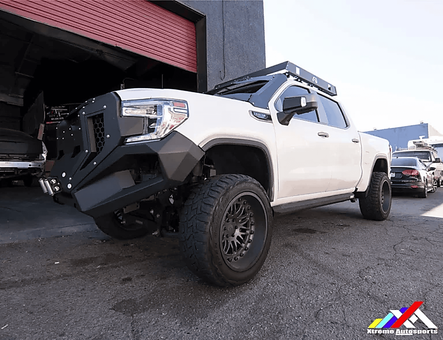 Off-road lifted white truck with aftermarket black front bumper and large tires.